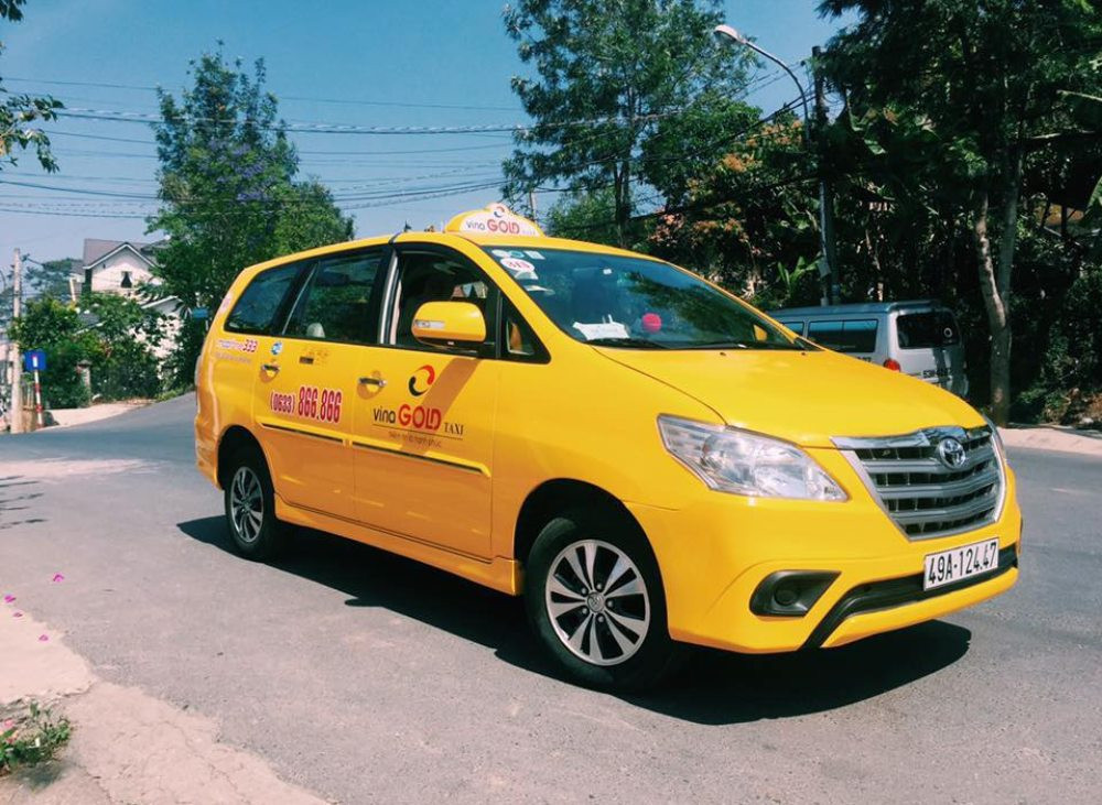 Chiếc taxi Vina Gold màu vàng nổi bật đậu trên con đường giữa khung cảnh xanh mát của Lâm Đồng