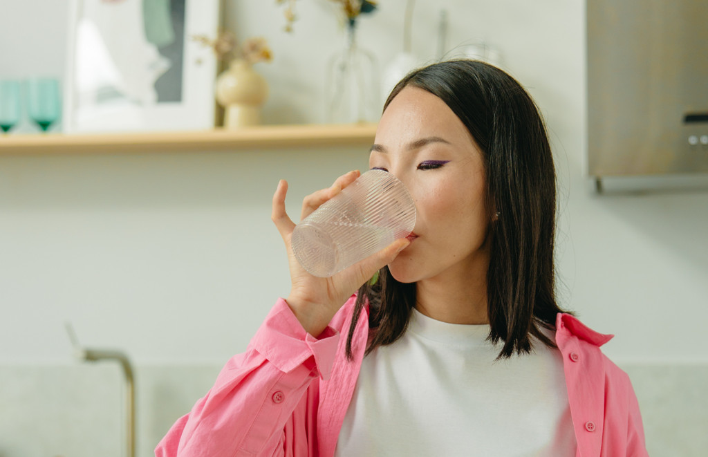 Một người đang uống nước cam trong ngày hè, biểu tượng của việc bổ sung vitamin cần thiết cho mùa hè.