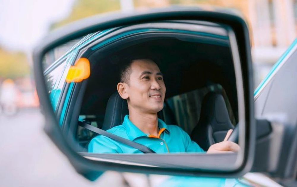 Tài xế taxi Xanh SM mỉm cười hài lòng bên xe điện VinFast, thể hiện sự hỗ trợ và phúc lợi tốt từ hãng