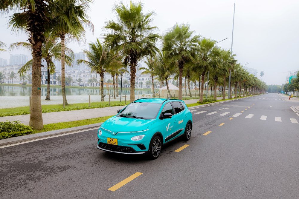 Xe taxi điện Xanh SM màu xanh cyan đặc trưng đang di chuyển trên đường phố, thể hiện sự khác biệt so với taxi truyền thống, góp phần vào hệ sinh thái giao thông bền vững.