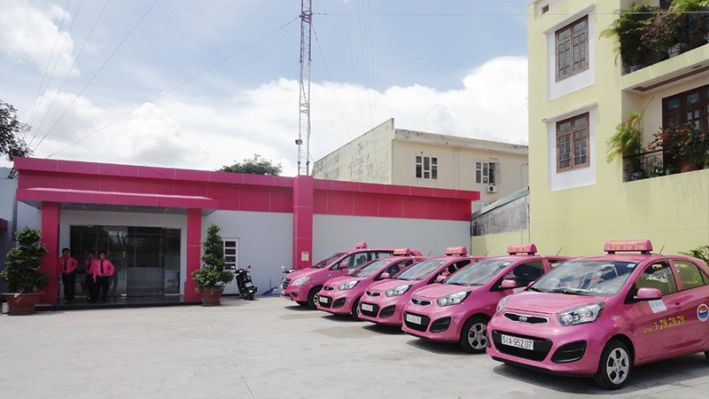 Xe taxi Hoàng Anh màu hồng đỗ gần một tòa nhà